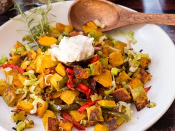 Diced and roasted Kabocha Squash with Peppers and leeks on a big white plate with a wood spoon. side view.