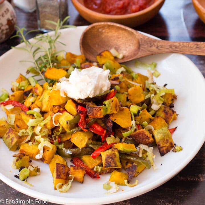 Diced and roasted Kabocha Squash with Peppers and leeks on a big white plate with a wood spoon. side view.