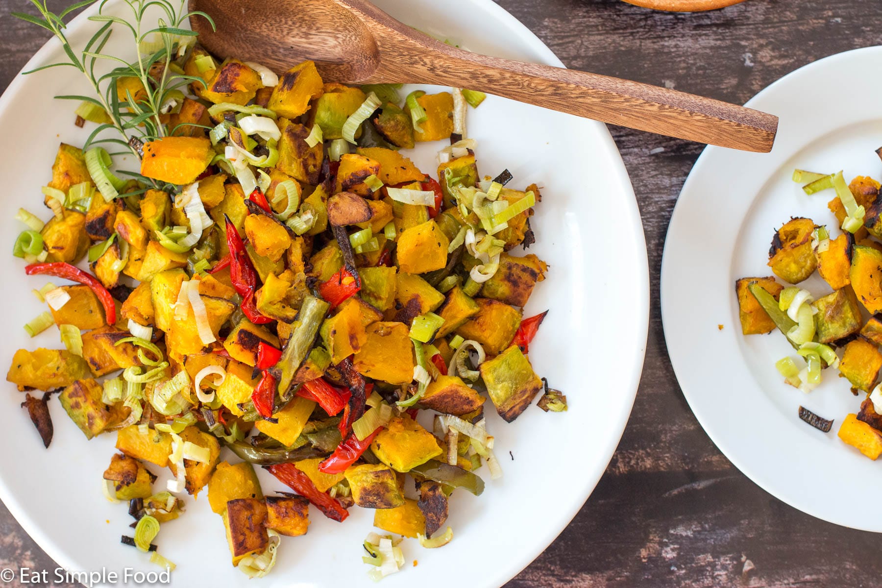 Diced and roasted Kabocha Squash with Peppers and leeks on a big white plate with a wood spoon. top view.