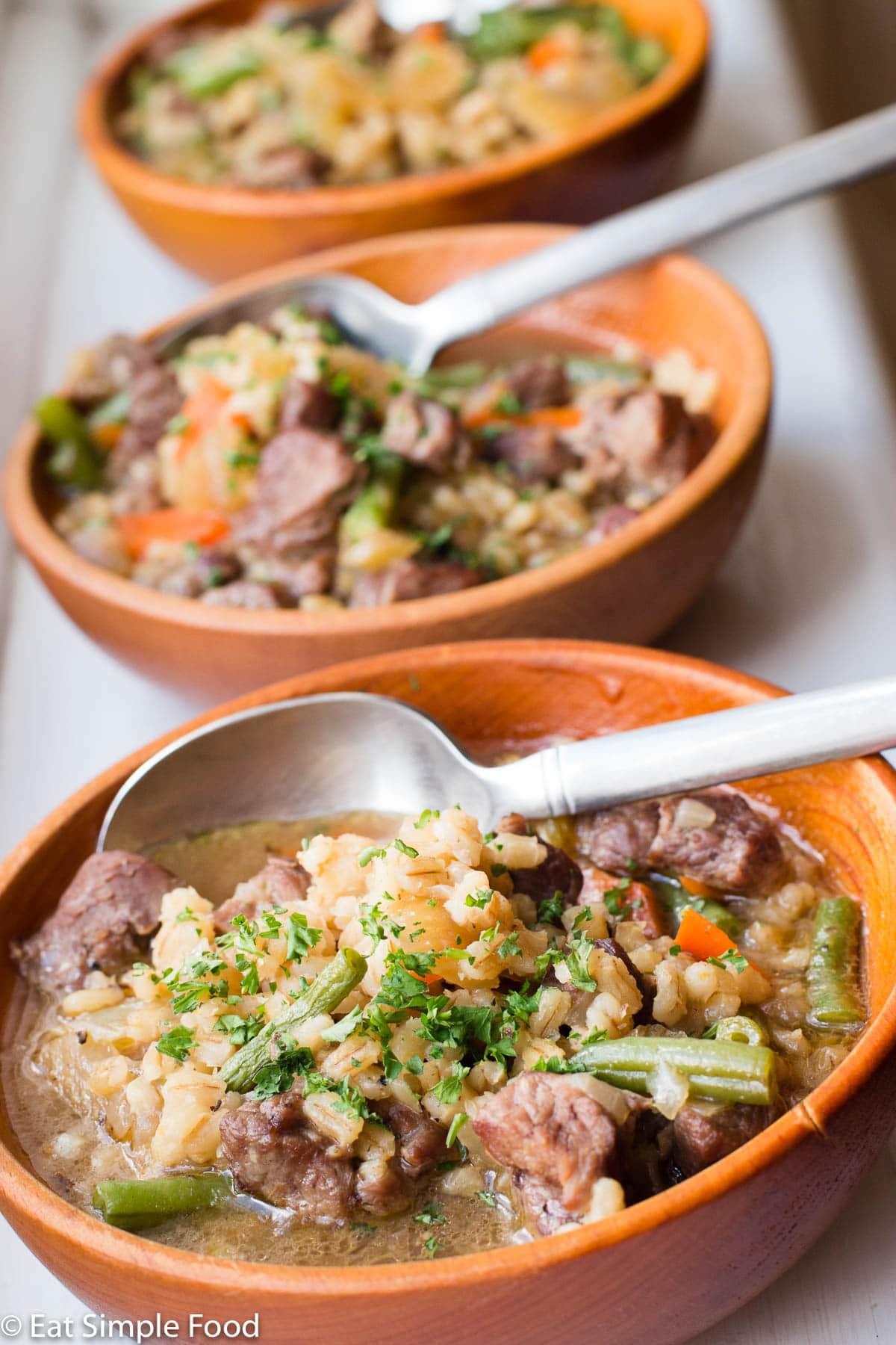 Lamb & Barley Stew in three wooden bowls with spoons sticking out.