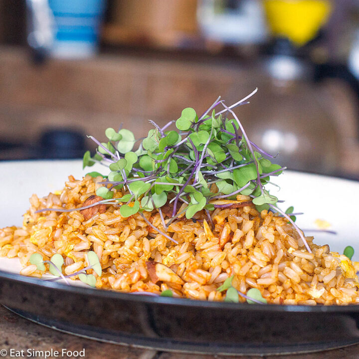 Brown Fried rice with scrambled eggs, toasted almonds, soy sauce, and fresh microgreen salad on top. White plate.