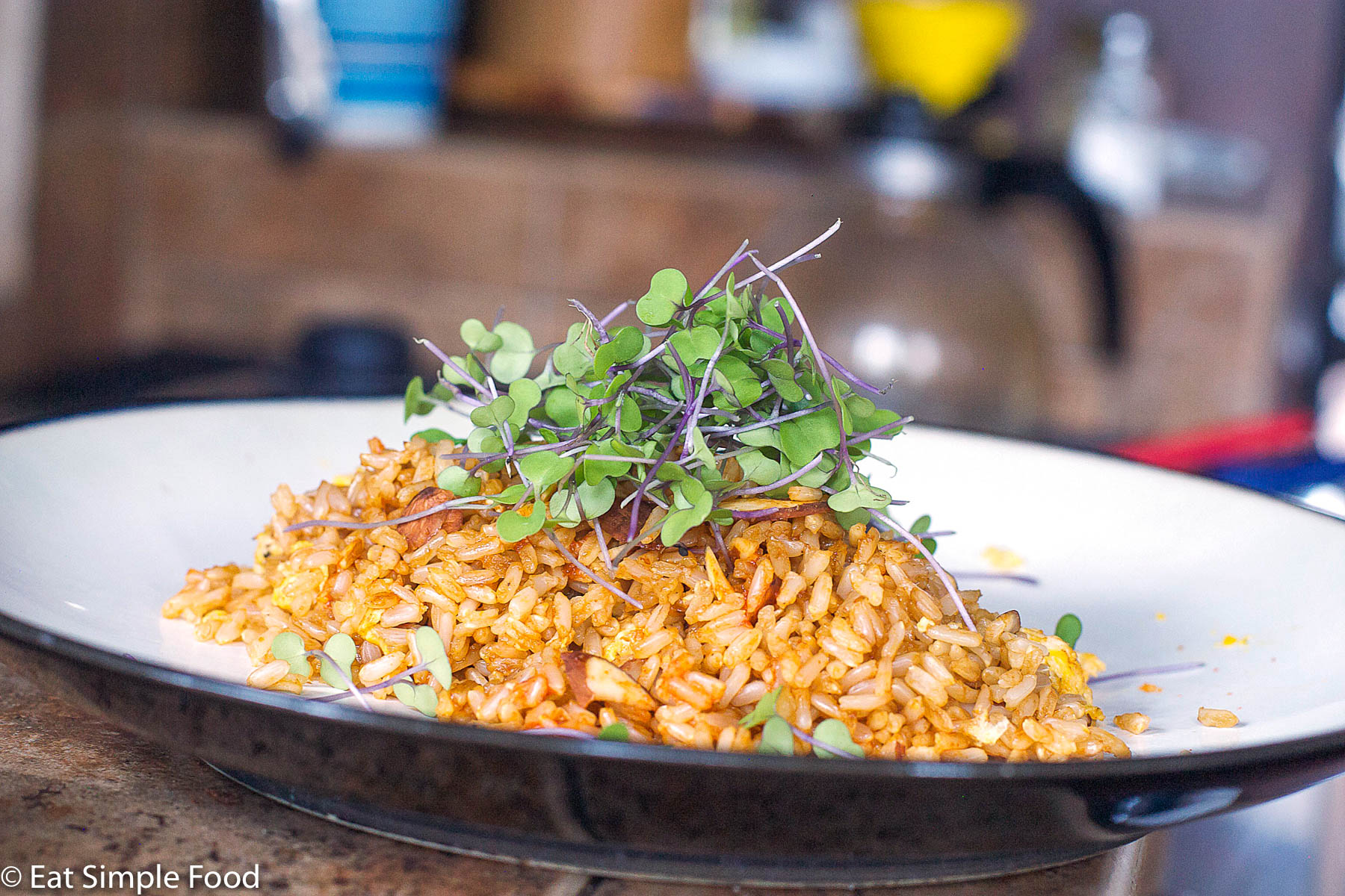Brown Fried rice with scrambled eggs, toasted almonds, soy sauce, and fresh microgreen salad on top. White plate.