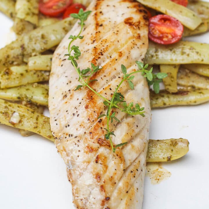 Close Up of Seared Amberjack Fish On A white plate on a bed of white pole beans.