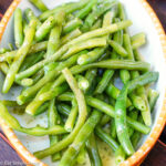 French green beans in a white oval platter with a tan trim tossed with dill.