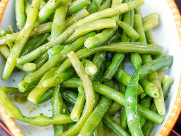French green beans in a white oval platter with a tan trim tossed with dill.