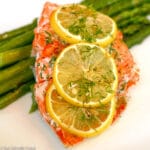 1 piece of cooked salmon topped with 3 lemon slices and chopped dill on a bed of asparagus.