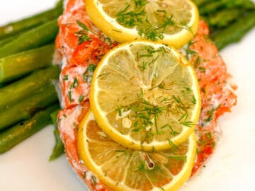 1 piece of cooked salmon topped with 3 lemon slices and chopped dill on a bed of asparagus.