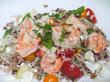 Lemon Shrimp, Capers, halved cherry tomatoes with sliced green onions over wild rice. Almond and Parmesan cheese garnish.