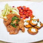 Sliced Pork Tenderloin browned with cilantro garnish on a white plate with roasted sweet potato coins with sour cream and chives, tomato salsa, and cucumber salad