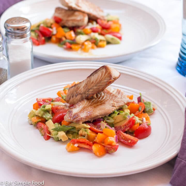 Two seared pieces of fish on a bed of ceviche salad (avocado, tomatoes, green onion, orange peppers. Top view with white plate