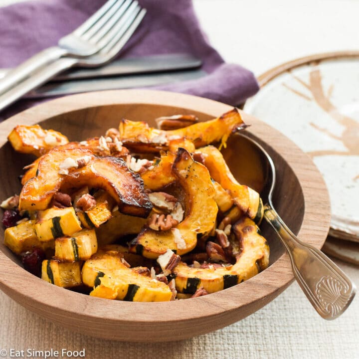Side View Browned half moons of delicata squash with cranberries and pecans in a brown bowl with a silver spoon