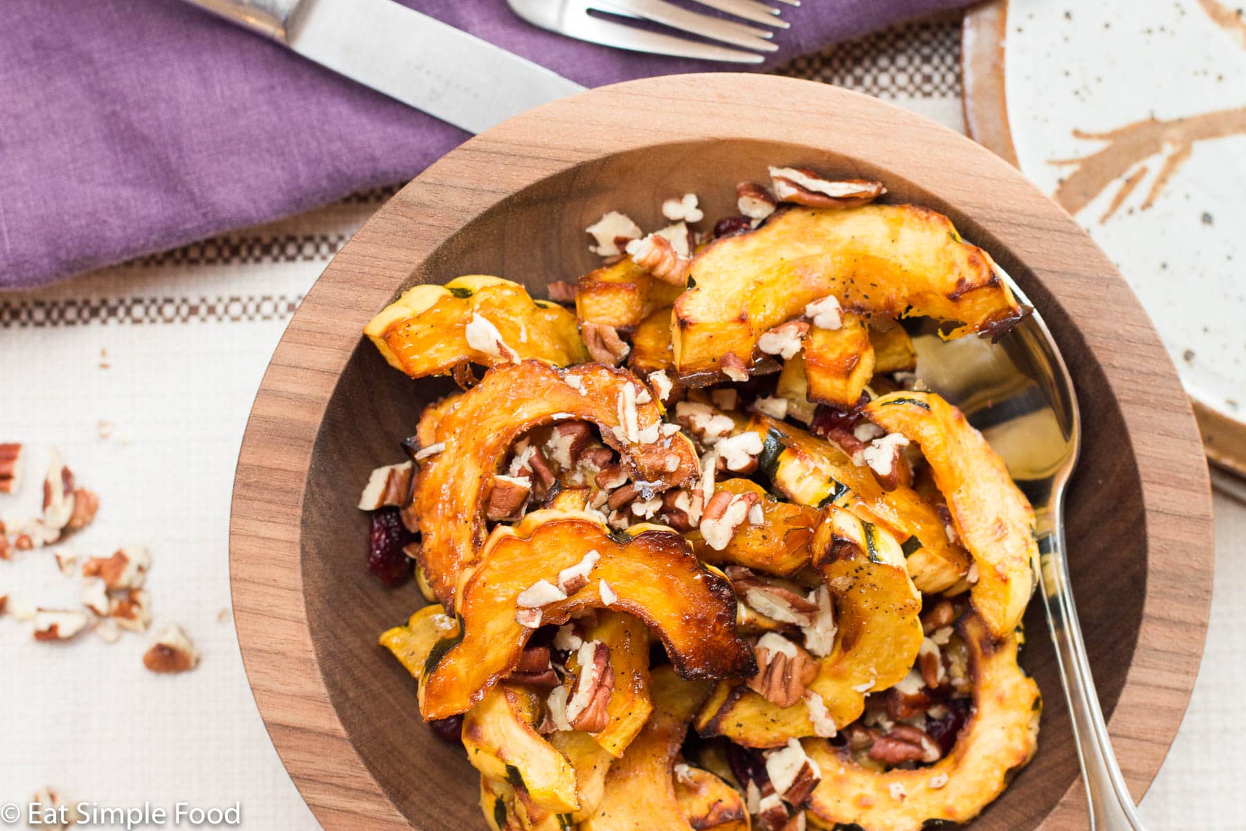 Top View Browned half moons of delicata squash with cranberries and pecans in a brown bowl.