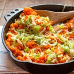 Mashed Carrots and Sliced Leeks in a cast iron pan with a wood spoon on a brown counter. side view