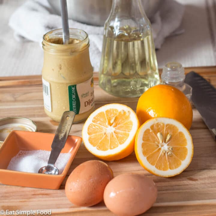 Ingredients for Mayonnaise - jar of mustard, whole lemons, vegetable oil, salt, and eggs. Bowl in the background with a whisk