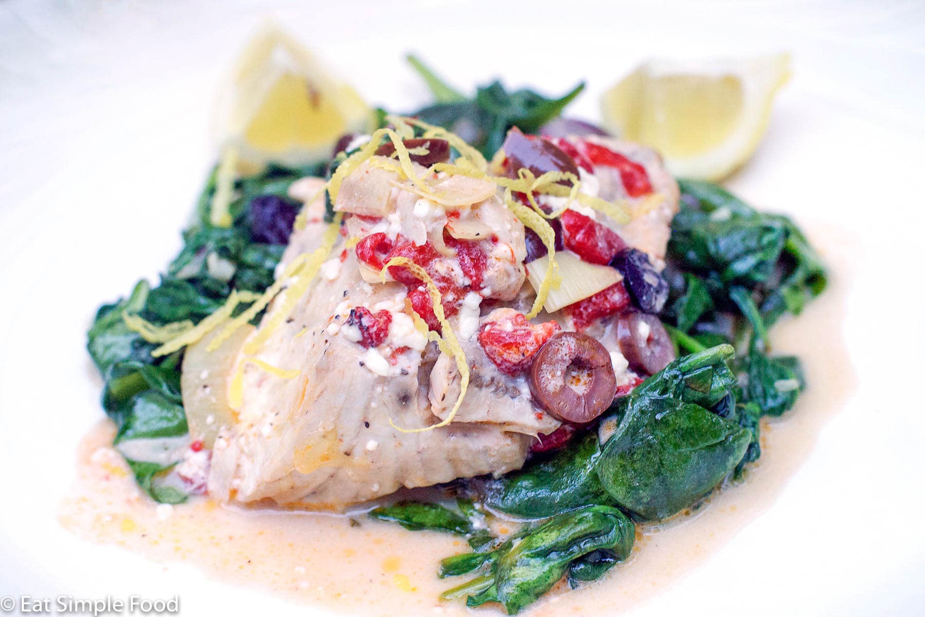 Amberjack Fish On A bed of spinach with kalamata olives, red peppers, lemon zest and lemon wedges.