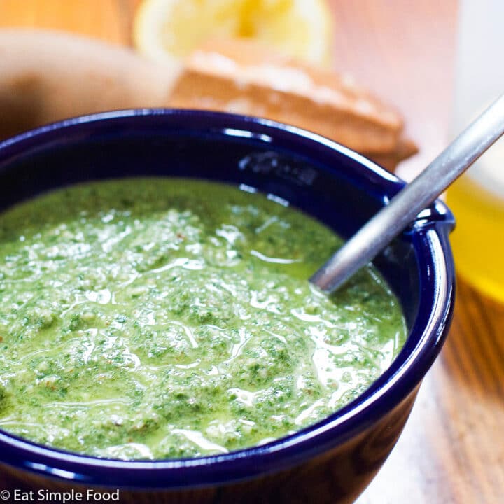 Blue bowl of green mint and pecan pesto blended with a silver spoon sticking out.