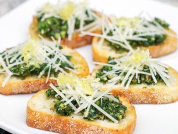 5 crostini (little toast) with green pesto and parmesan sprinkled on the top. Garnished with lemon zest. On a white plate