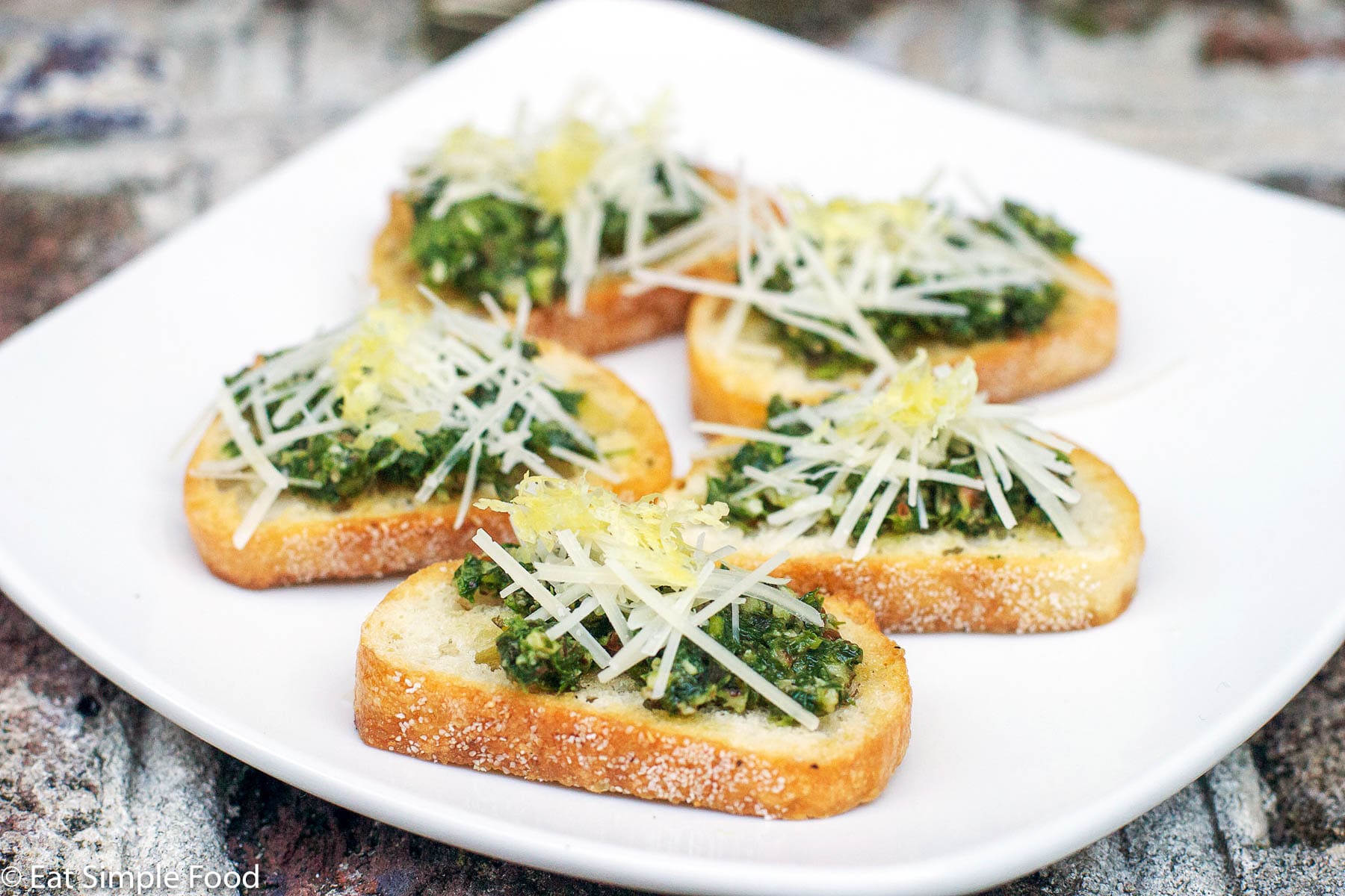 5 crostini (little toast) with green pesto and parmesan sprinkled on the top. Garnished with lemon zest. On a white plate