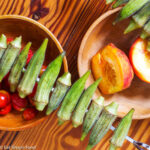 Raw Okra on a Silver skewer over a bowl of cherry tomatoes and halved peaches.