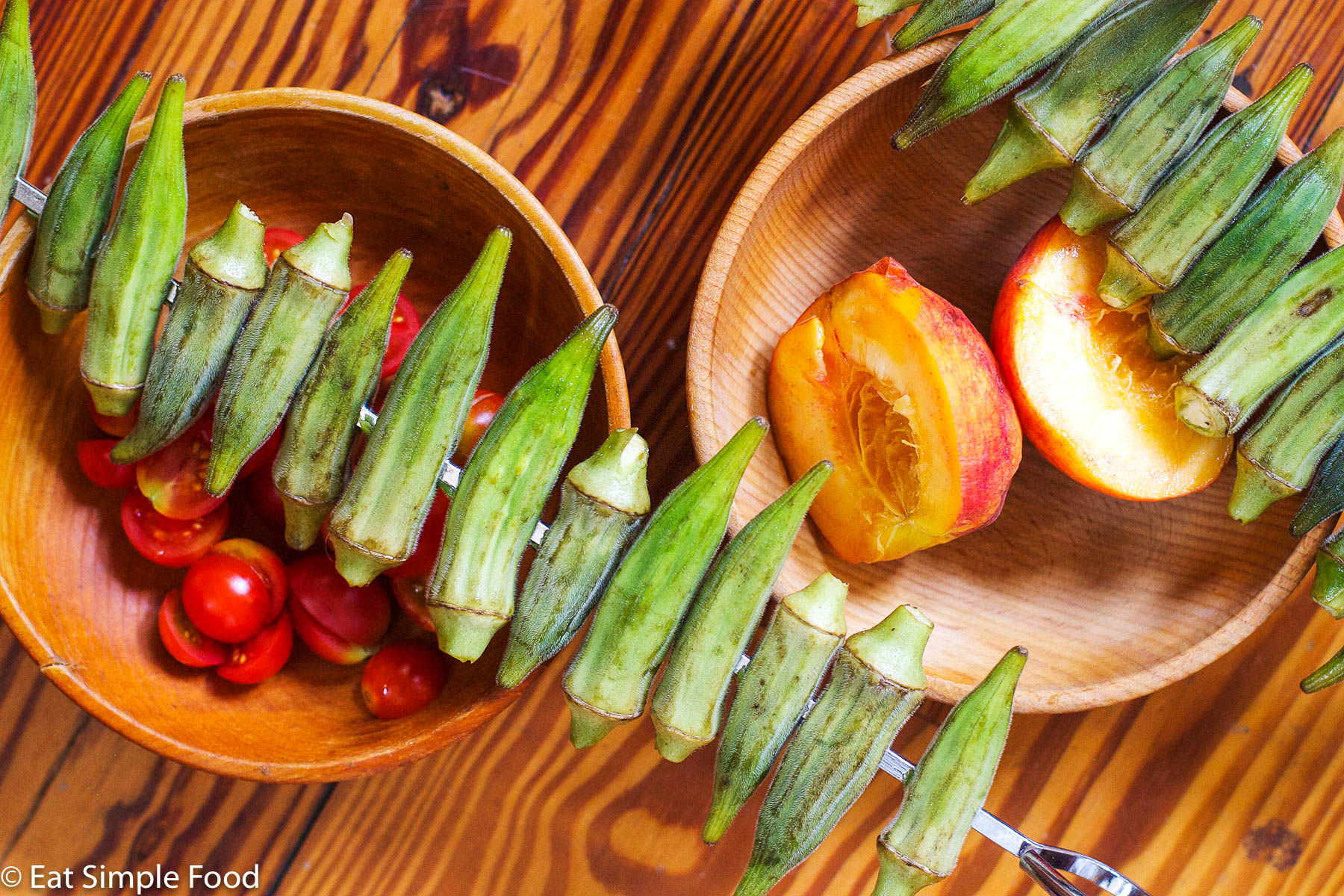Raw Okra on a Silver skewer over a bowl of cherry tomatoes and halved peaches.