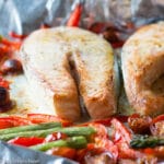 2 pieces of raw salmon fillets on an aluminum sheet pan with asparagus, sliced red peppers, and halved cherry tomatoes.