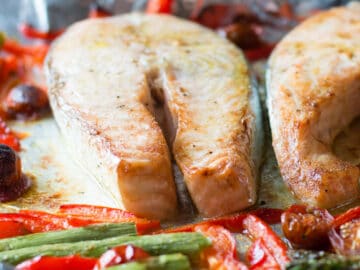 2 pieces of raw salmon fillets on an aluminum sheet pan with asparagus, sliced red peppers, and halved cherry tomatoes.