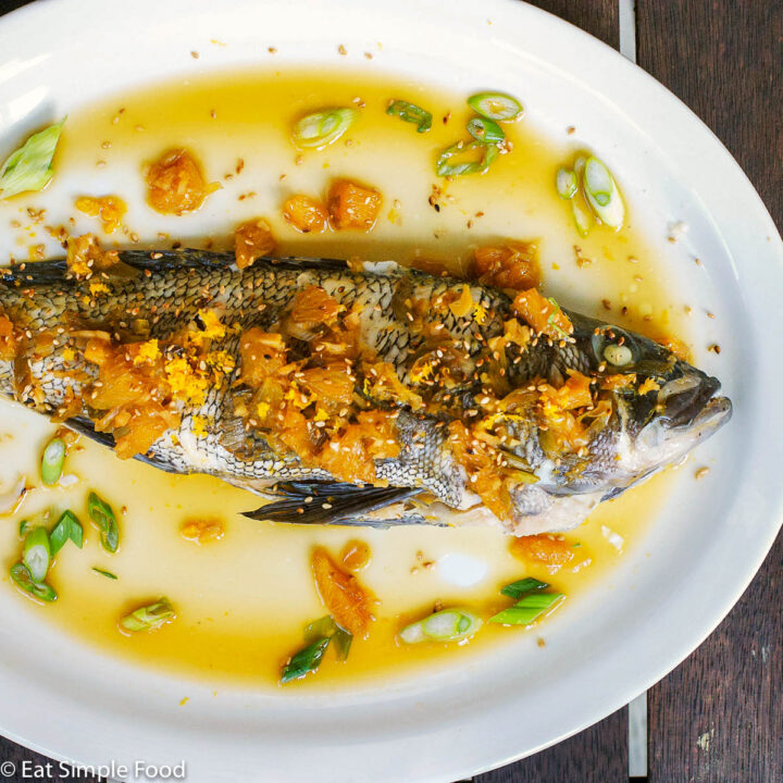 Whole Fish on a platter sitting on white rice and green beans. Topped with Orange sauce and garnished with sliced green onions.