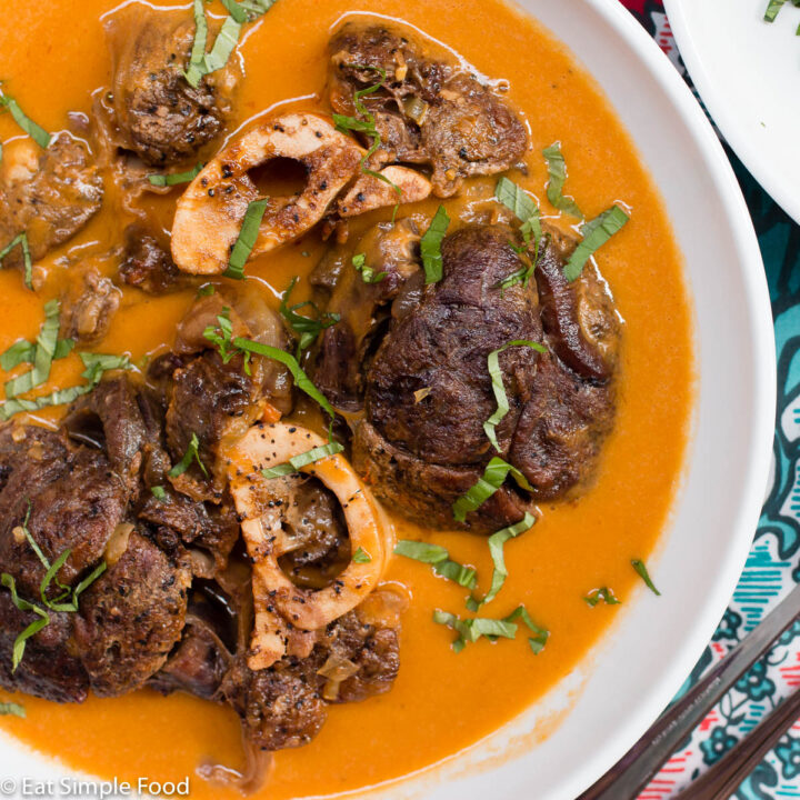 Top view of shallow bowl of beef shanks with marrow in an orange vegetable puree. Garnished with basil.