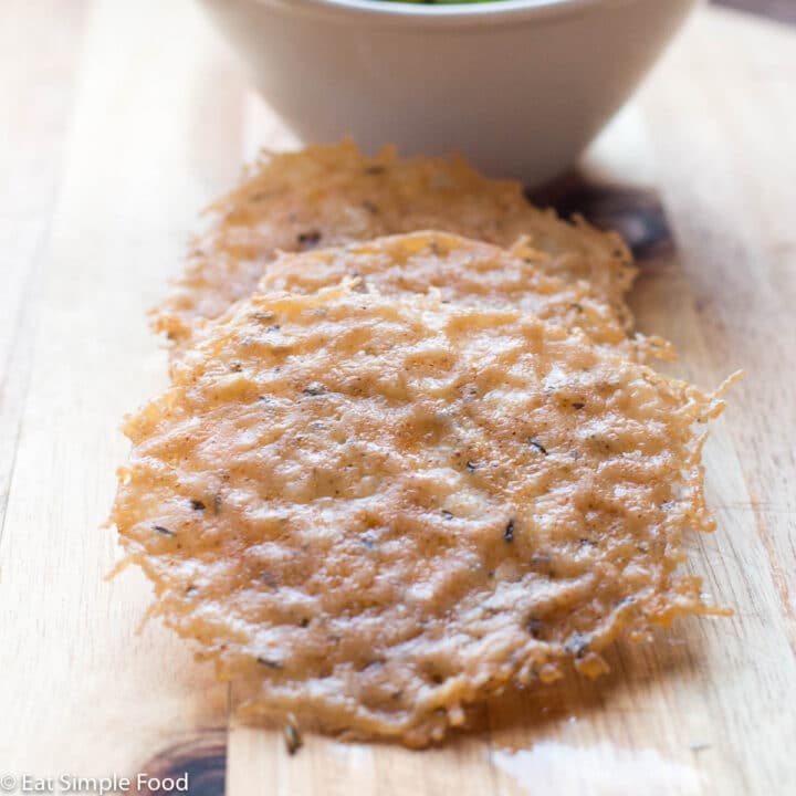 3 Parmesan Crisps with specks of thyme on a Wood Cutting Board