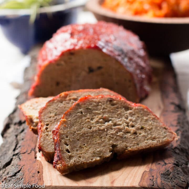 Turkey Meatloaf on a wood cutting board with 3 pieces sliced. Mashed Sweet potatoes in background and small plant in blue bowl.