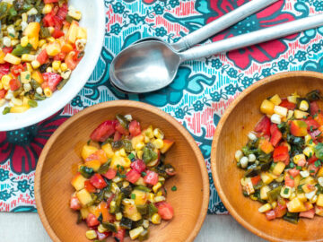 2 wood bowls and one larger white bowl of chunks of peaches, tomato, and corn salsa. Spoons on the side.