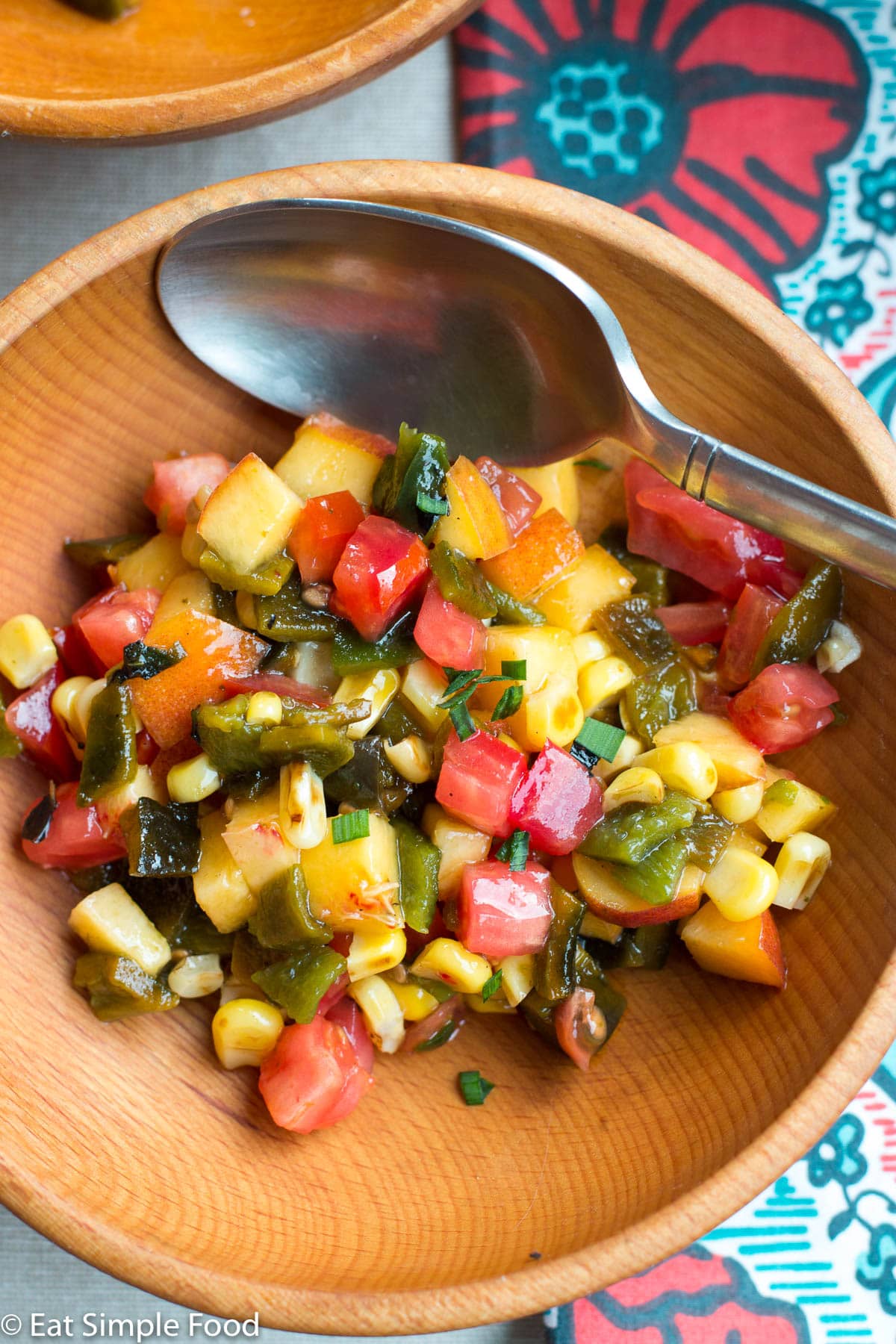 Wood bowl of chunks of peaches, tomato, and corn salsa. Spoons on the side. Top view.