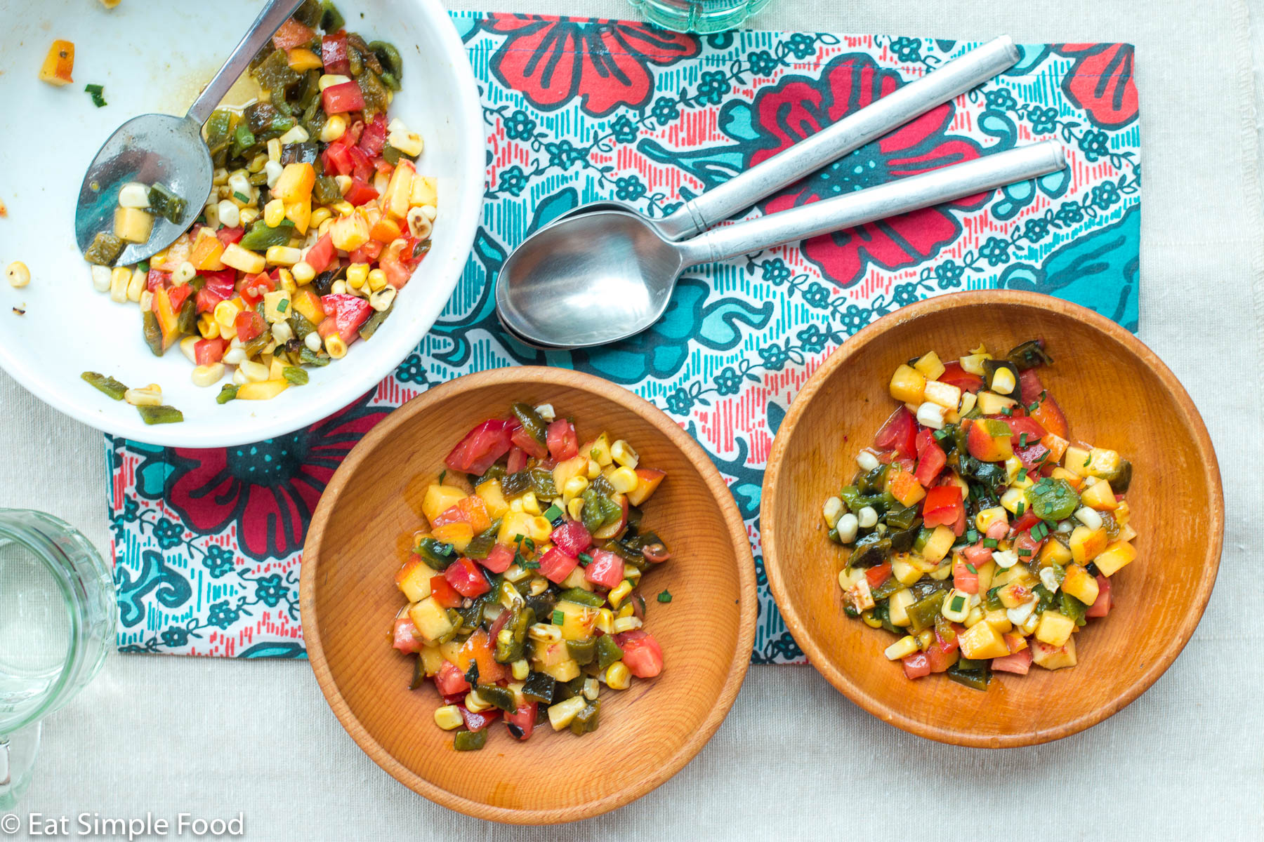 2 wood bowls and one larger white bowl of chunks of peaches, tomato, and corn salsa. Spoons on the side.