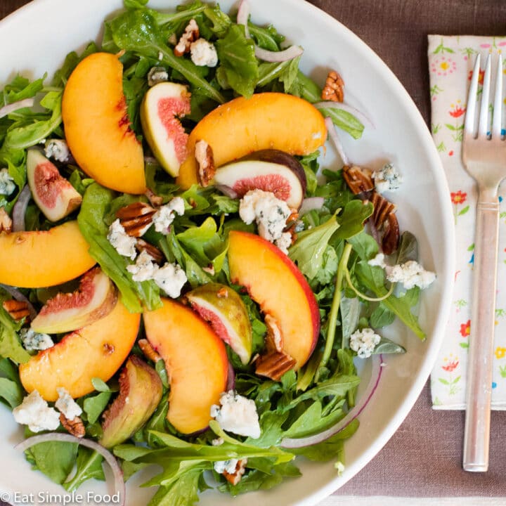 Sliced Peaches, quartered figs, chunked pecans, and crumbled blue cheese on a deep plate with fork and napkin. Top view.