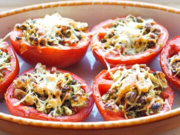 6 tomato halves filled with wild rice, basil pesto, pine nuts, and feta cheese with Parmesan cheese broiled on the top. Close up.