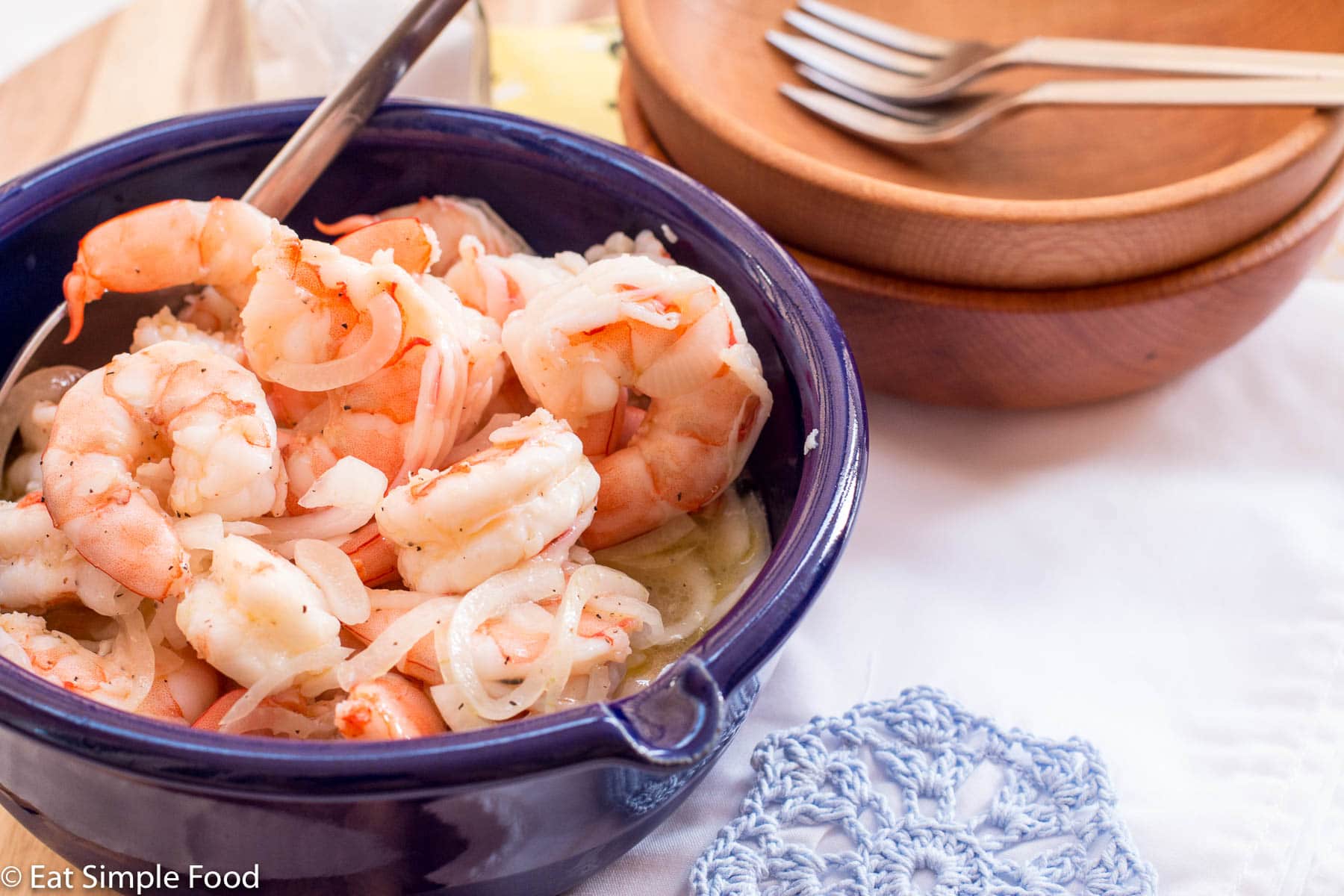 Cooked Pickled Shrimp with thin sliced onions In a blue bowl with a spoon sticking out. 2 wood bowls with small forks on the side.