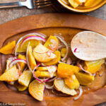 Yellow Golden Beets roasted and sliced and tossed with red onions and a dressing. On a wood plate with a wood spoon.
