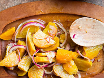 Yellow Golden Beets roasted and sliced and tossed with red onions and a dressing. On a wood plate with a wood spoon.