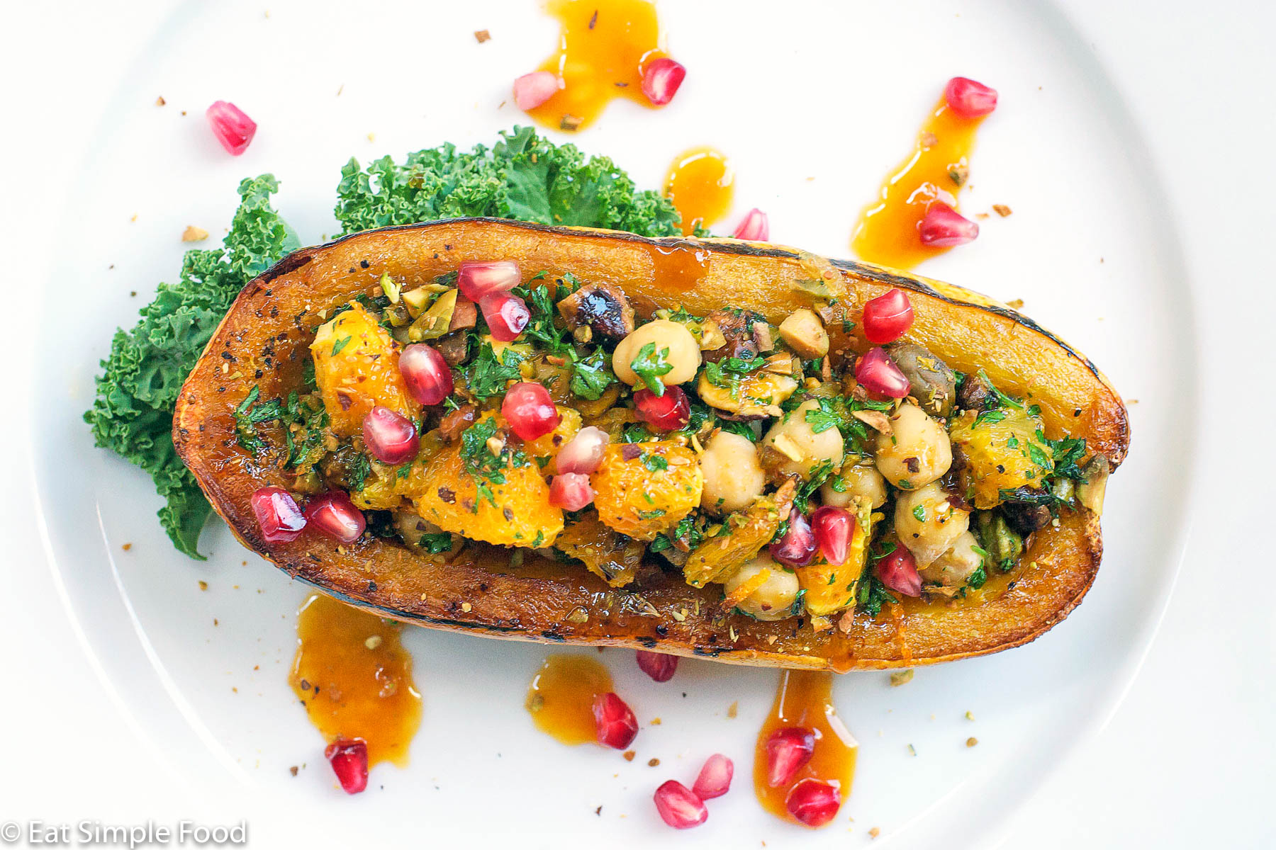 Half a delicata squash hollowed out and roasted and stuffed with parsley and pistachio pesto and garnished with pomegranate kernels on a white plate with orange sauce.