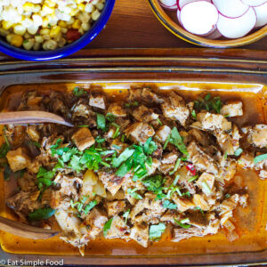 Shredded Mexican Spiced Pork On a Brown Plate with Wood Tongs and a Chopped Cilantro garnish.