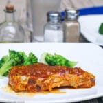 Pork Chop with red Tomato Ginger Curry sauce on a white square plate with broccoli behind it.
