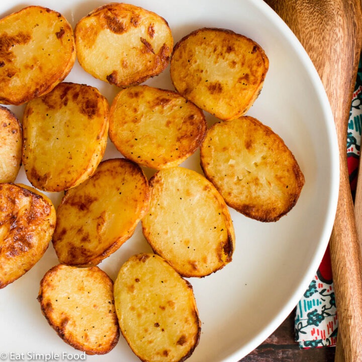 Roasted brown, peeled and halved Yukon Gold Potatoes on a round white platter. Top view.