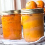 one quart size jar of preserved lemons. one quart size jar of preserved clementines. On a white kitchen towel. fresh clementines in background.