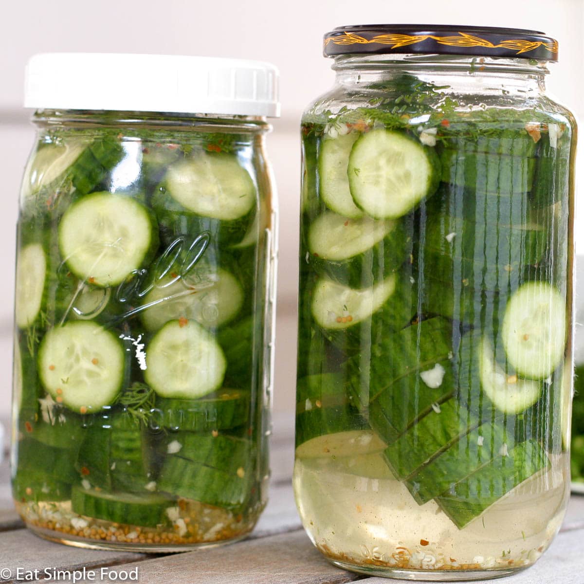 2 Mason Jars filled with sliced Pickles and vinegar and red pepper flakes and garlic. Side view.