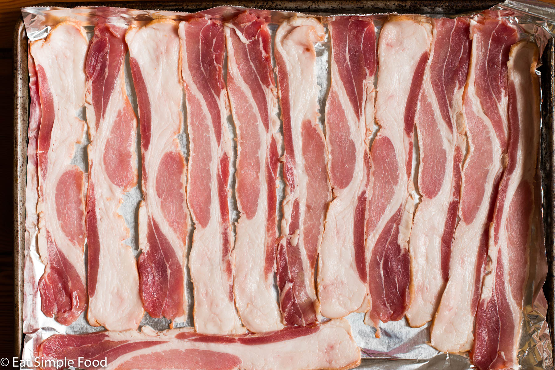 Raw bacon snuggled together on a sheet pan. Top view, close up.
