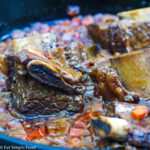 Close Up of Beef Short Ribs in a brown sauce with diced carrots, bones sticking out. side view.
