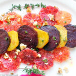 Blood Oranges & Roasted Yellow and Red Beets on a white plate with thyme and walnuts sprinkled over the top.