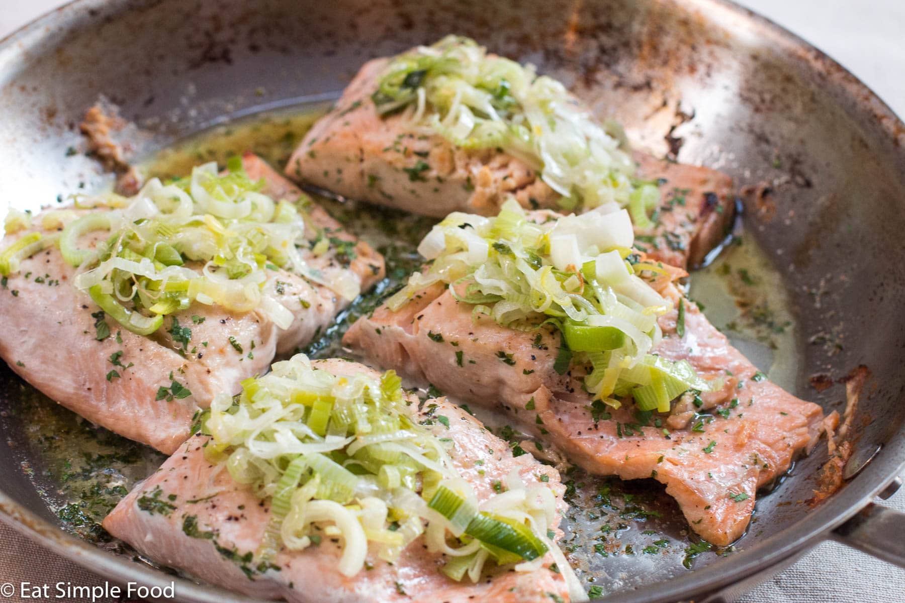 4 Roast Salmon pieces with Buttery Leeks On Top In a Stainless Steel Pan