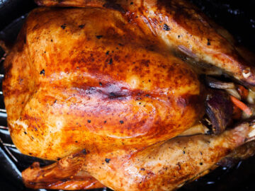 Top view of dark golden brown whole roasted turkey in a black roasting pan.