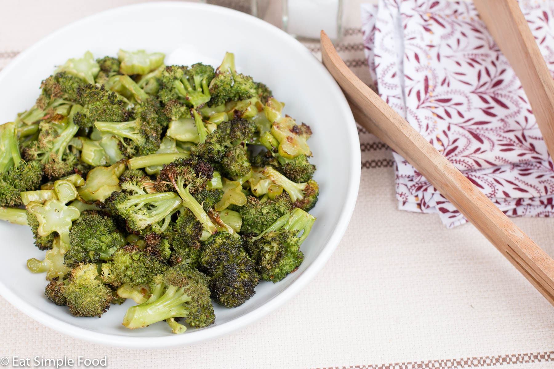White Bowl of Browned Roasted Broccoli Florets with wood tongs. side view